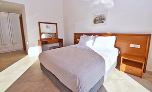 Ein Hotelzimmer mit einem großen Bett, einem Nachttisch aus Holz, einem Beistelltisch, einem Schminktisch und einem Bilderrahmen an der Wand.