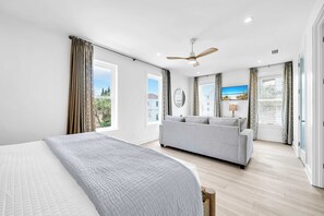 Ein Schlafzimmer mit Bett, einer Schlafcouch, Deckenventilator und großen Fenstern.