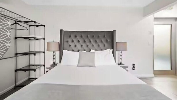 Un dormitorio moderno con una cama grande, un cabecero gris capitonado, dos mesitas de noche con lámparas y una estantería empotrada a la izquierda.