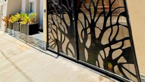 Una casa moderna de dos pisos con fachada color beige, un gran portón negro con diseño de árbol y un ventanal en el nivel superior.
