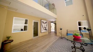 Un interior espacioso con techo alto, balcón y zona de comedor con mesa de vidrio.