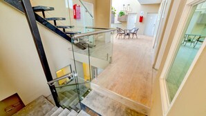 Un interior moderno con una escalera de cristal, una zona de comedor con sillas y una mesa, y un extintor visible.