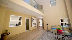 Un interior espaiós amb un sostre alt, una taula de vidre amb cadires i una escala que porta a un nivell superior.