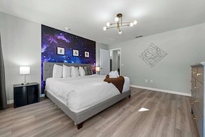 A modern bedroom with a galaxy-themed wall mural, a grey bed, a bedside table with a lamp, and a geometric wall art piece. - 12 min to Disney • Movie Theater • Pool (Davenport)
