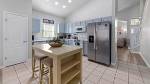 Una cuina moderna amb armaris de blau clar, un refrigerador d'acer inoxidable i una illa central amb una planta.