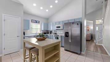 A modern kitchen with light blue cabinets, a stainless steel refrigerator, and a central island with a plant.