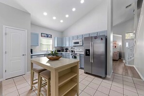A modern kitchen with light blue cabinets, a stainless steel refrigerator, and a central island with a plant. - 12 min to Disney • Movie Theater • Pool (Davenport)