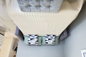Une chambre dotée d’un grand lit, d’une tête de lit capitonnée et de deux coussins décoratifs.