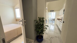 Een hal met een bed, een potplant en een keukenhoek.