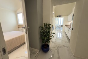 A hallway with a bed, a potted plant, and a kitchen area. - Exclusivity, Luxury and Sea View with 2 Bedrooms (Alassio)