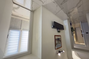 A room with a ceiling featuring a marble-like pattern, a window with blinds, a mounted television, and a framed picture on the wall. - Exclusivity, Luxury and Sea View with 2 Bedrooms (Alassio)