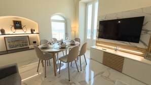 Een moderne eetruimte met een marmeren vloer, een grote flatscreen televisie en uitzicht op zee door een groot raam.