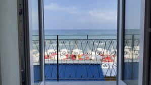 Uitzicht vanuit een balkon met een hekwerk, op een strand met parasols en boten.