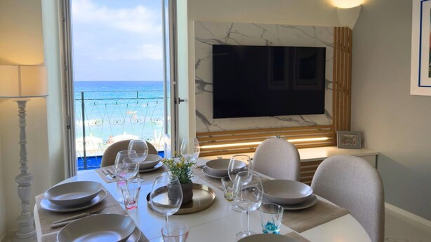 Een eetgedeelte met uitzicht op zee, een wandtelevisie en een moderne tafelschikking.