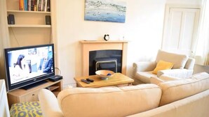 Ein Wohnzimmer mit Sofa, Fernseher, Kamin und Bücherregal.