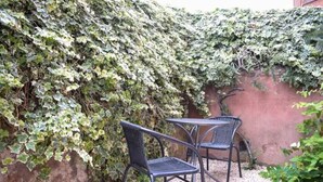 Eine Terrasse mit zwei Metallstühlen und einem Tisch, umgeben von einer dicht bewachsenen Mauer mit Efeu.