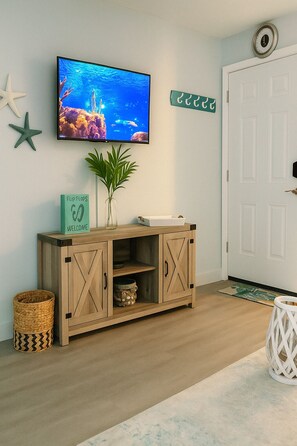 Ein Zimmer mit einem Holzkasten, einem Fernseher der eine Unterwasserwelt zeigt, einem Willkommensschild, einer Pflanze und einer Tür mit einer Nummer.'