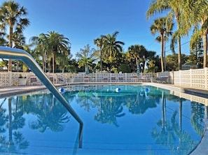 Ein Swimmingpool mit klarem, blauem Wasser, umgeben von Palmen und einem weißen Zaun.