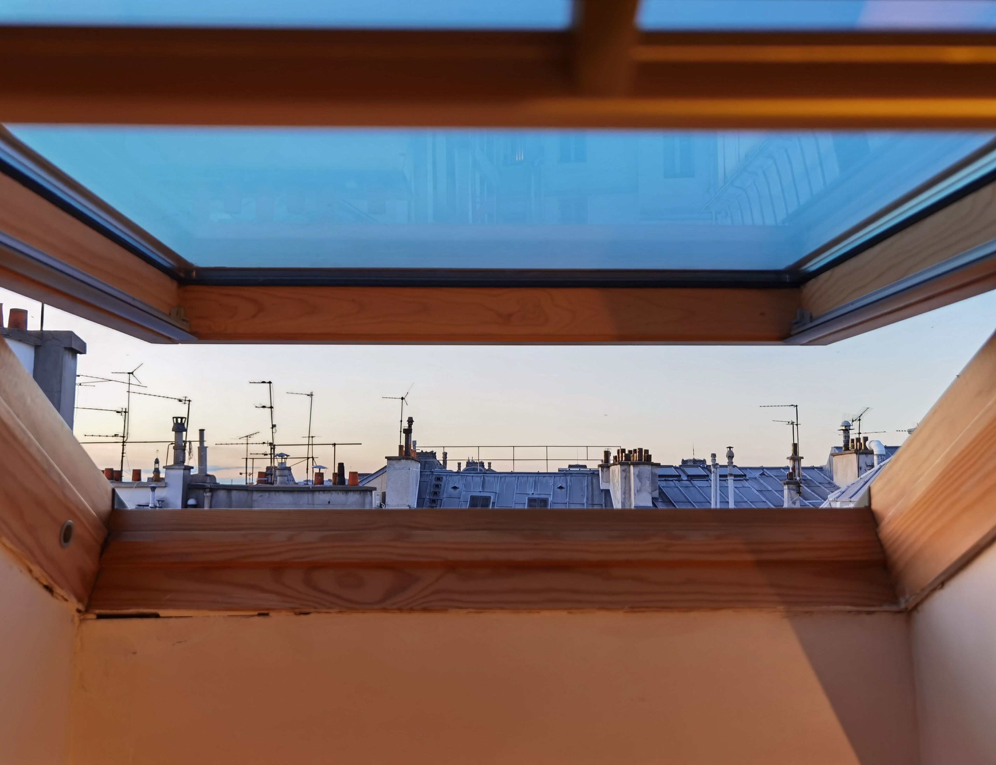 A skylight in a room with a view of rooftops and antennas.
