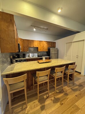 A kitchen with wooden cabinets, a granite countertop, and a central island with bar stools. - Serene 2-bedroom condo in Eagle-Vail, perfect for a fun getaway (Avon)