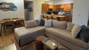 A modern living room with a sectional sofa, ottomans, a dining table, and a kitchen in the background. - Serene 2-bedroom condo in Eagle-Vail, perfect for a fun getaway (Avon)