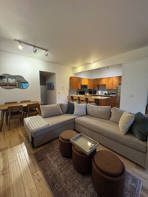 A modern living room with a sectional sofa, ottomans, a dining table, and a kitchen in the background. - Serene 2-bedroom condo in Eagle-Vail, perfect for a fun getaway (Avon)
