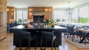 A modern kitchen with a large island, wooden cabinets, and a view of the outdoors. - The Napa Sanctuary • Vineyard Views • Hot Tub (Napa)