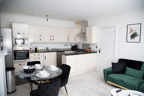 A modern kitchen with white cabinets, a dining table with black chairs, and a green sofa. - Luxury 2 BED near tube station (London)