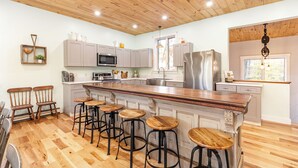 A spacious kitchen with wooden flooring, a large island with stools, grey cabinets, stainless steel appliances, and a wooden ceiling. - Lockes Hill Retreat - Close to Gunstock (Gilford)