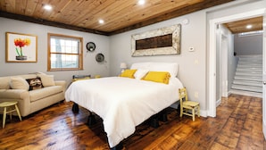 A bedroom with a large bed, wooden flooring, a window, a sofa, and a staircase. - Lockes Hill Retreat - Close to Gunstock (Gilford)
