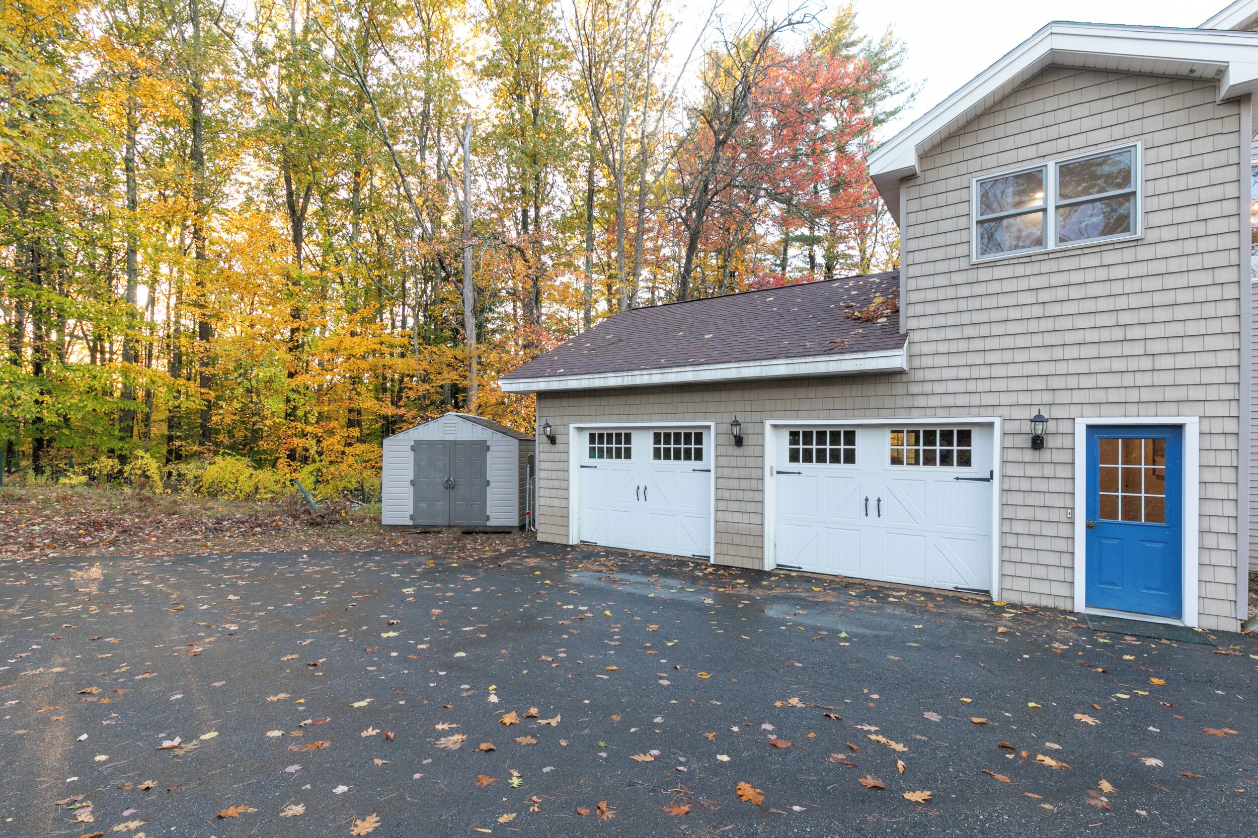 Un bâtiment à deux étages, doté d’un garage et d’une remise, entouré d’arbres aux feuilles d’automne.