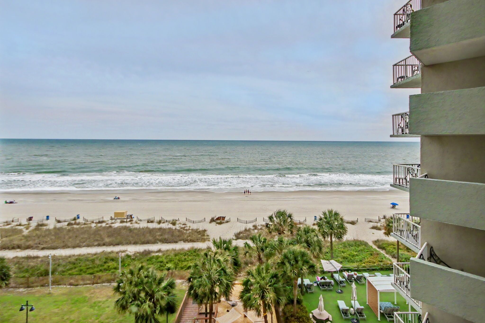 A beachfront hotel with balconies, a sandy beach, and palm trees.