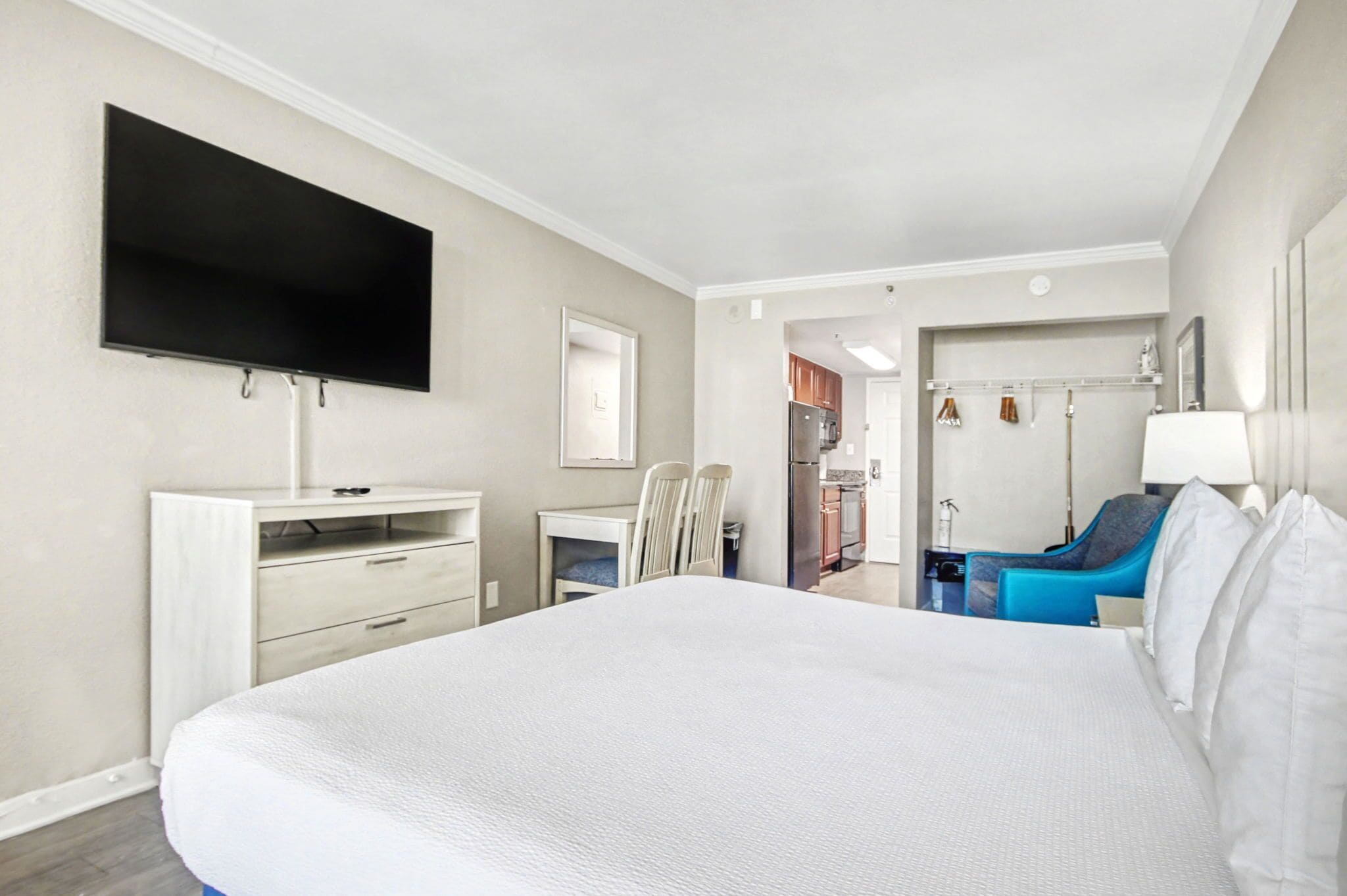 Une chambre d’hôtel comprenant un lit, un téléviseur fixé au mur, un bureau avec des chaises, une salle de bain avec douche et une armoire.