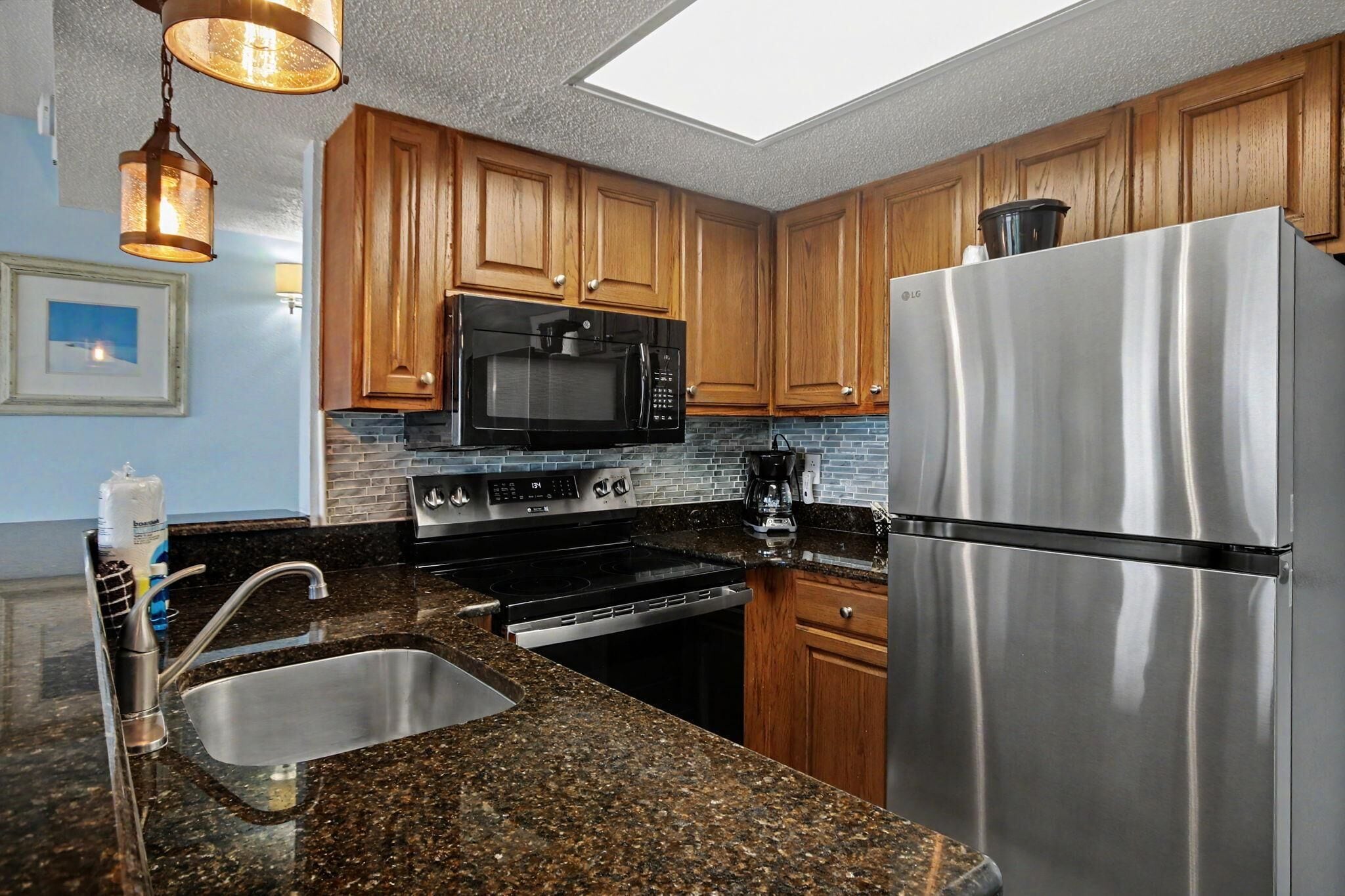 A modern kitchen with granite countertops, stainless steel appliances, wooden cabinets, and pendant lighting.