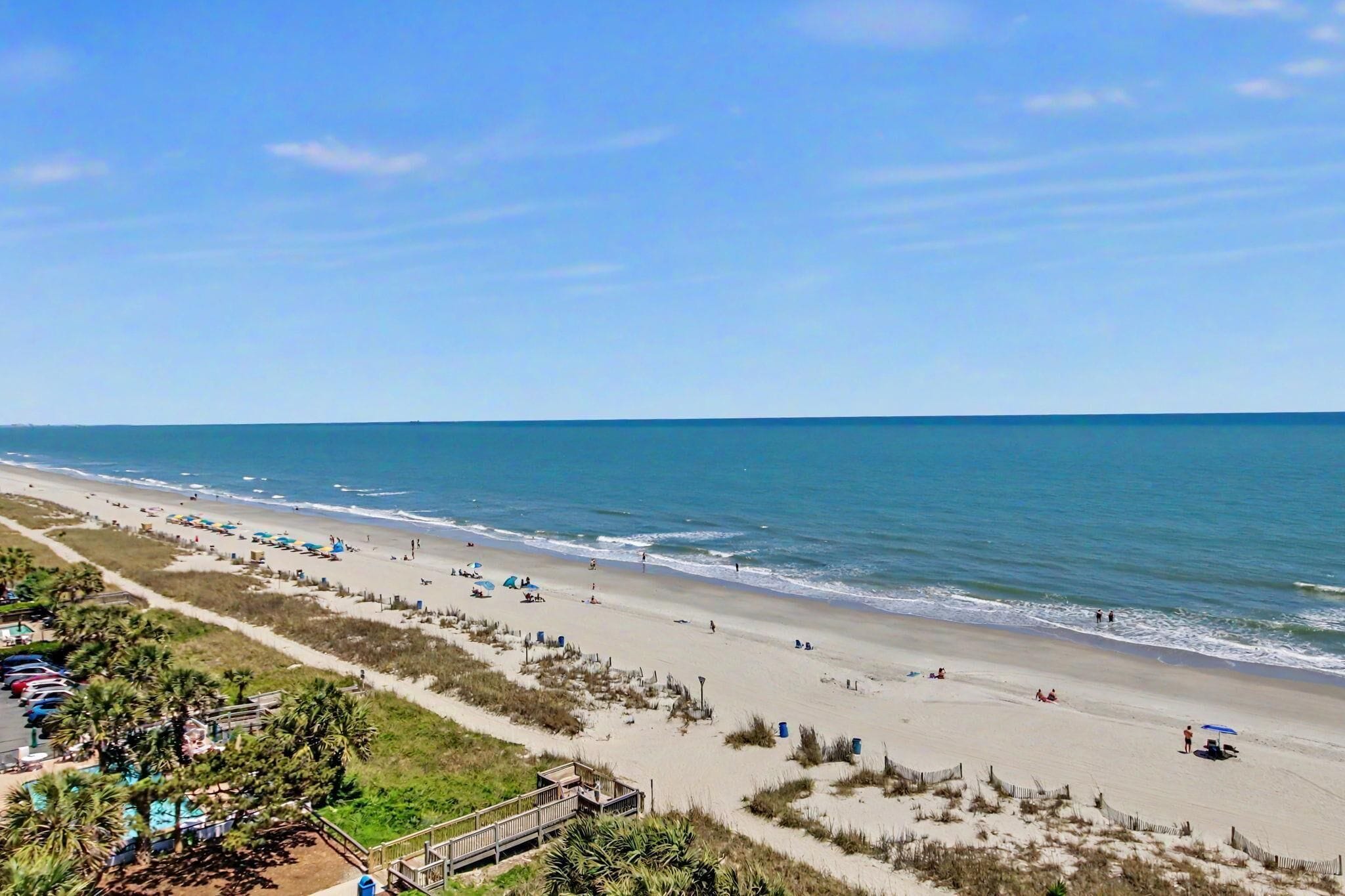 A beach with a boardwalk, umbrellas, and beach chairs.