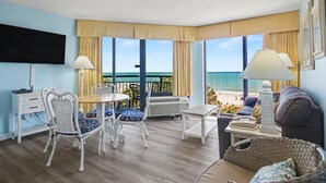 Una habitación con balcón, zona de comedor, sofá y televisor.