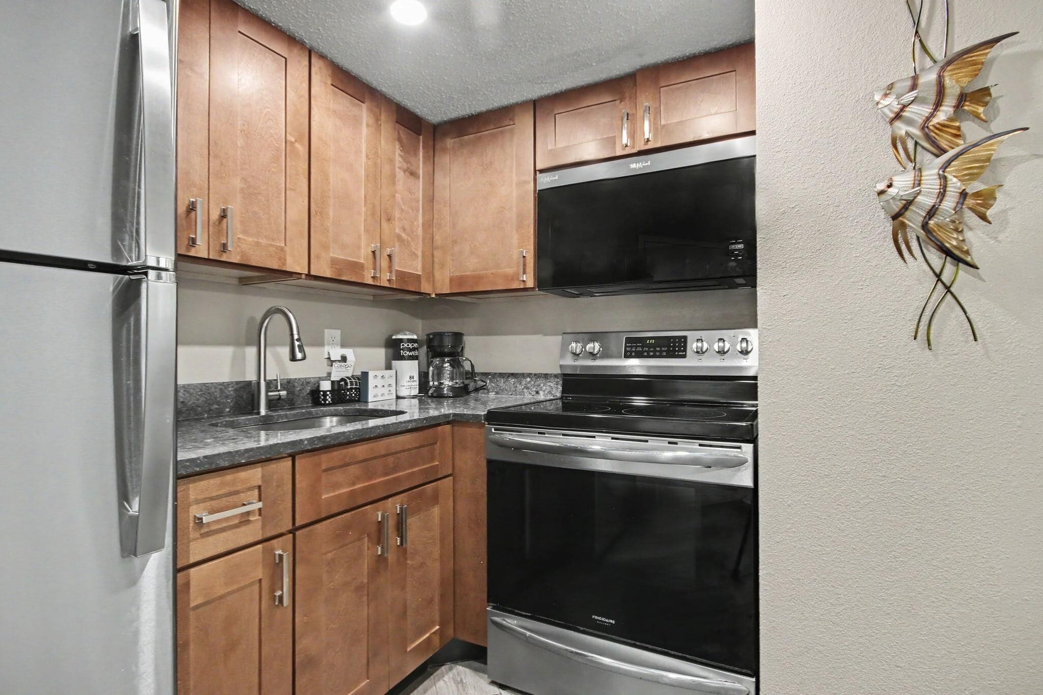 Una cocina con armarios de madera, electrodomésticos de acero inoxidable, una cafetera y un cuadro decorativo con peces.