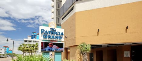 Un hotel llamado "The Patricia Grand" con un letrero, la entrada a un estacionamiento y un cielo despejado.