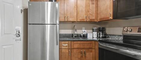 A kitchen with wooden cabinets, a stainless steel refrigerator, a microwave, and a stove.