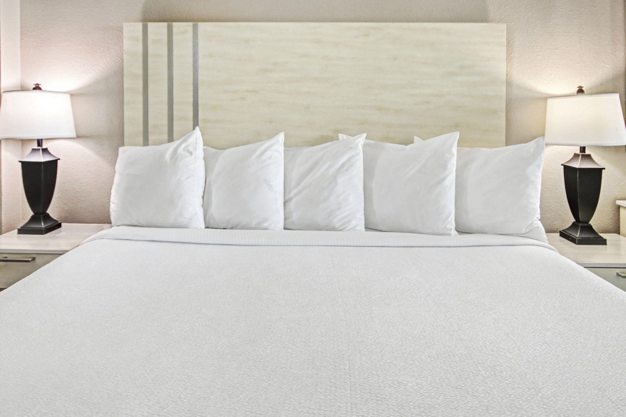 A neatly made bed with white linens and pillows, flanked by two bedside tables with lamps.