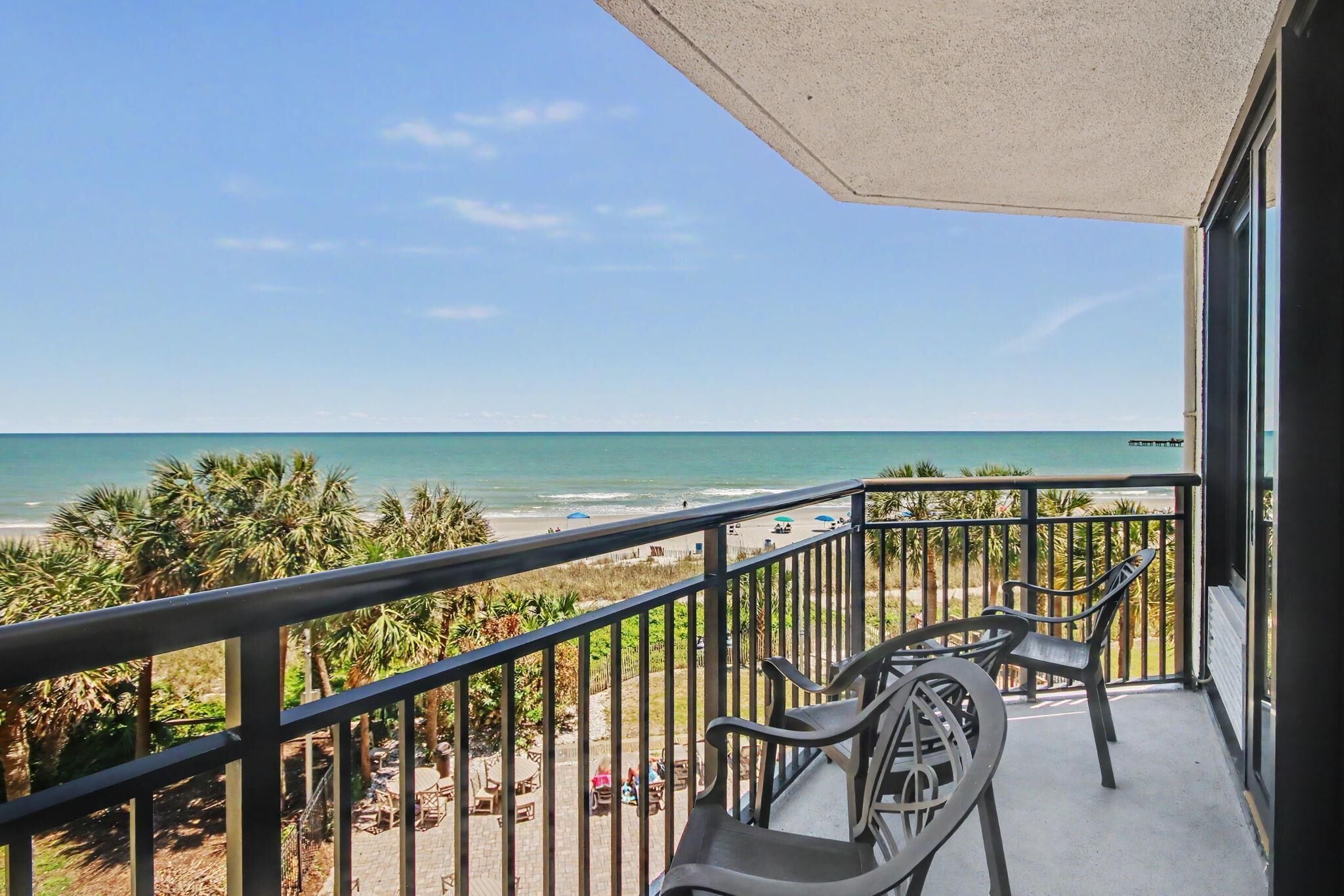 A balcony with a view of the beach, palm trees, and a pier.