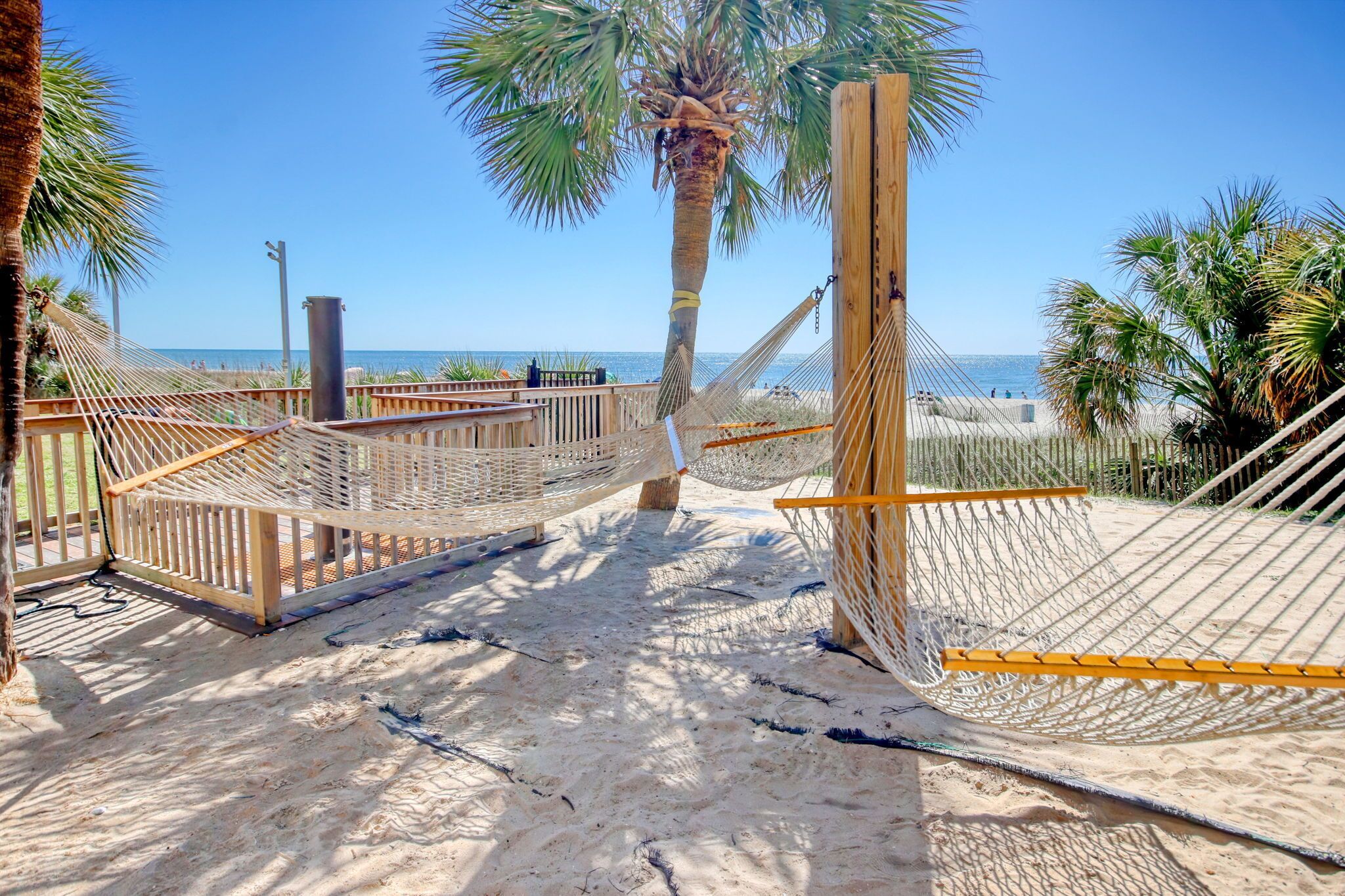 A beach with hammocks and a wooden fence.