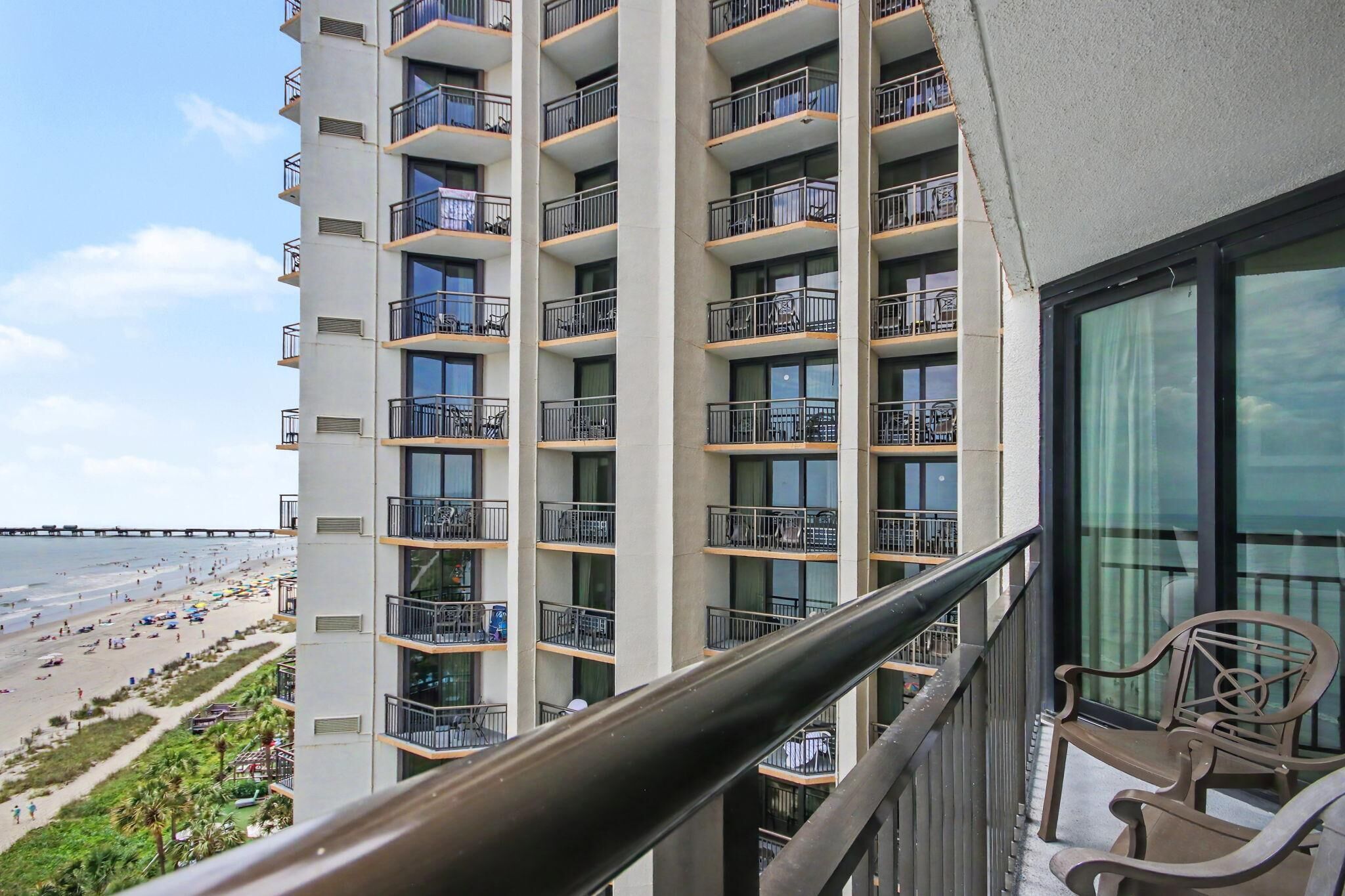 A high-rise hotel with multiple balconies, a beach view, and a clear sky.