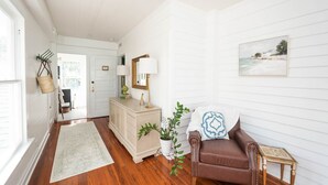 A spacious living room with hardwood flooring, a brown leather armchair, a white sofa, a beige dresser, and a white door leading to another room.