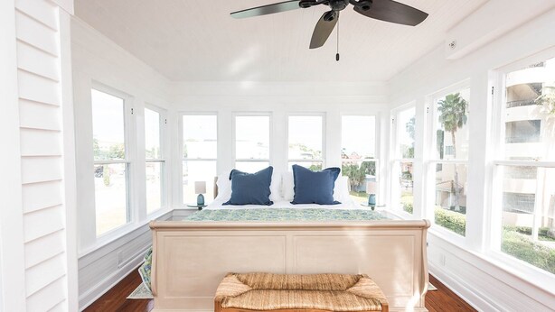 A bright room with a large bed, a ceiling fan, and multiple windows.