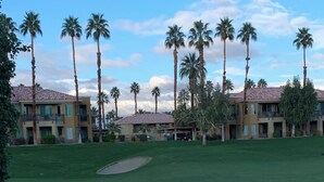 A golf course with a water feature in the foreground, palm trees, and a building with balconies in the background. - Coachella @ Marriott’s Palm Desert Villas II, One bedroom/Kitchen on golf course (Palm Desert)