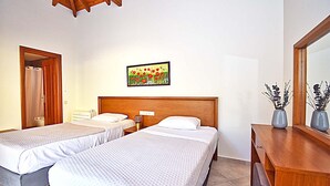 Quarto de hotel com duas camas de solteiro, cabeceira de madeira, mesa de cabeceira, espelho e um quadro na parede.