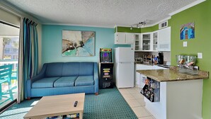 A compact living space with a sofa, coffee table, kitchenette, and a painting on the wall. - Casa Del Mar 118-welcome to Keylois (Galveston)
