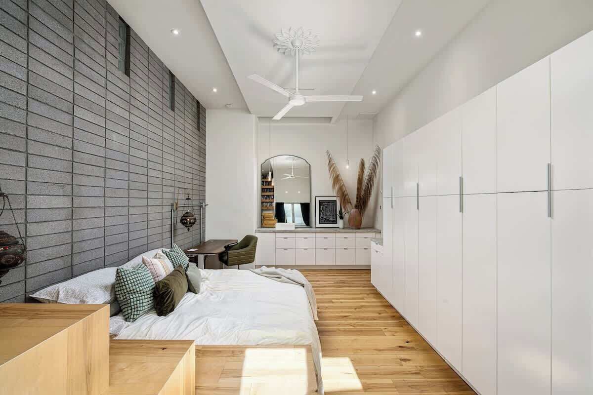 Ein modernes Schlafzimmer mit Bett, Holzboden, einem weißen Kleiderschrank und einem Schreibtisch mit Stuhl.