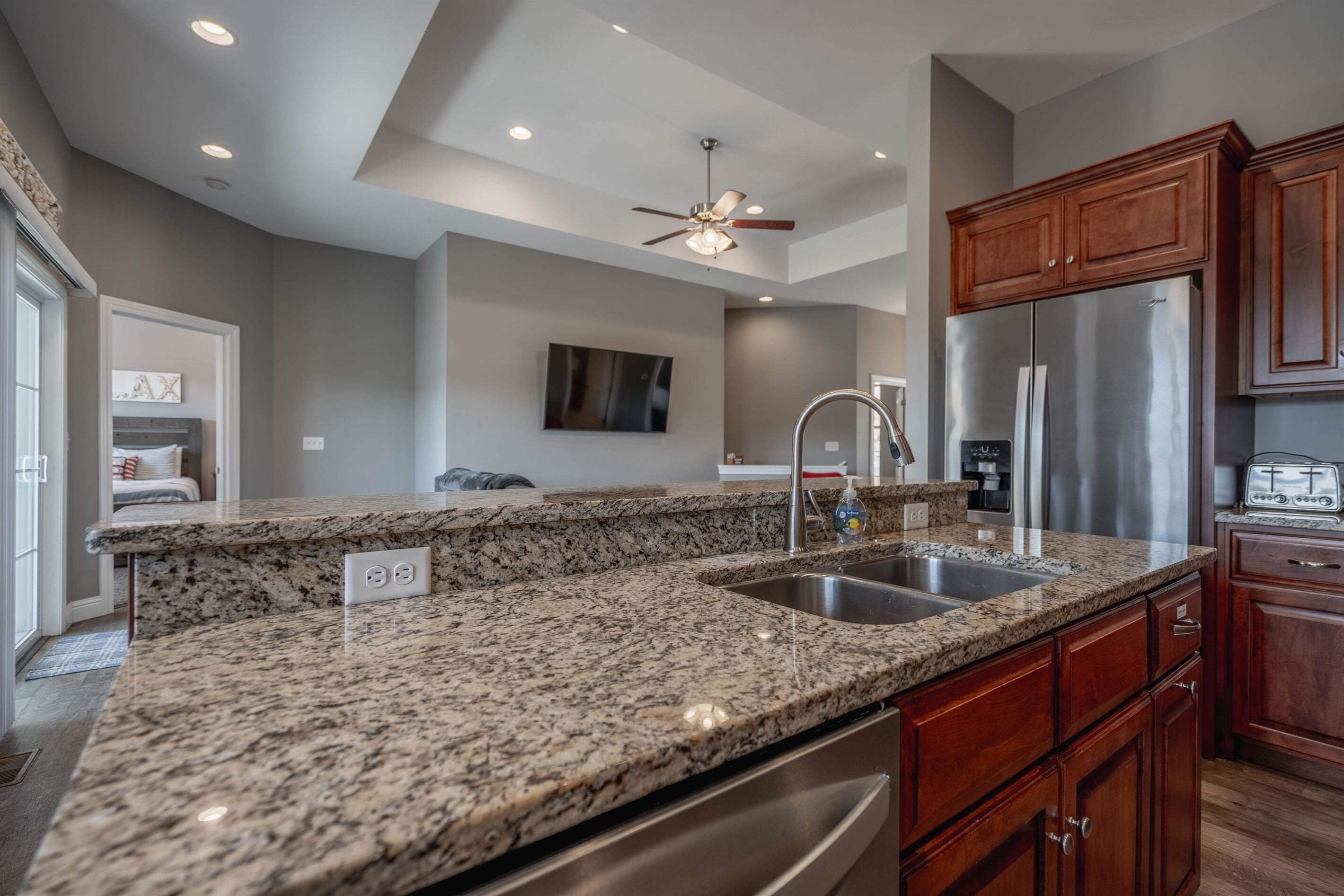 A kitchen with granite countertops, stainless steel appliances, wooden cabinets, and a ceiling fan.